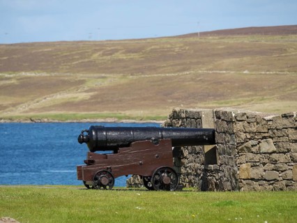 Historic cannon in front of a stone wall with sea view and a hill in the background, old cannons on