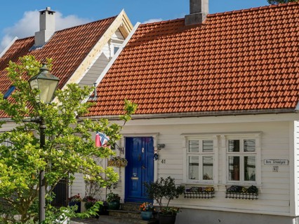 White house with red tiled roof and blue entrance, green plants and lantern in the foreground,
