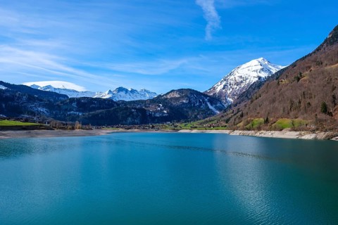 Lake Lungern surrounded by snow-capped mountains and green hills under a blue sky, Lungern,