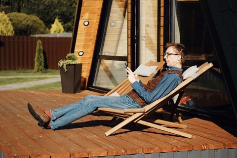 Middle aged man using smartphone while resting on terrace of wooden cabin in a sunny day