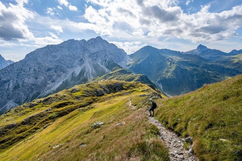 Mountaineer on a hiking trail on a grassy mountain ridge, idyllic mountain landscape with green