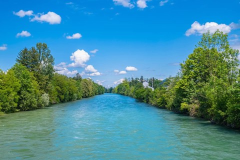 A calm river surrounded by green trees under a blue sky with fluffy clouds, Emmen, Lucerne,