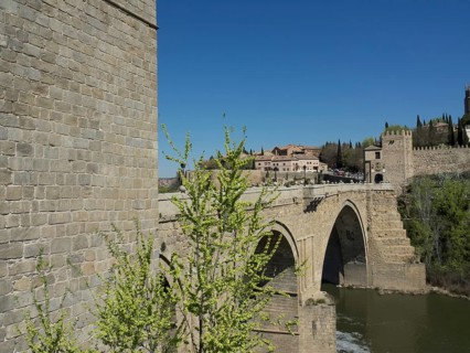 Historic stone bridge crossing a river, surrounded by green vegetation and clear blue sky, historic