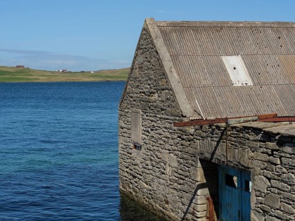 Stone clad building on the water's edge with sea and sky in the background, old stone house on the