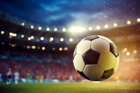 A soccer ball is in the air on football stadium, surrounded by players on a field during the game,