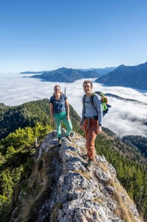 Two hikers at Ettaler Manndl, view over mountain landscape and sea of clouds, high fog in the