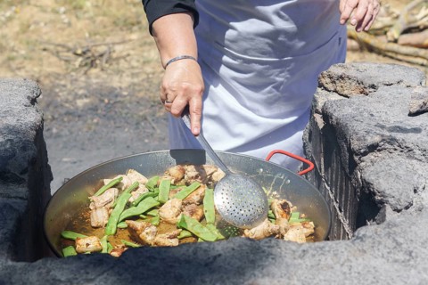 Closeup of a woman cook in a white apron preparing a typical Valencian paella on the fire in the