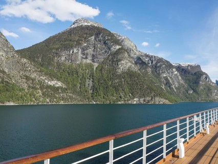 Ship deck in front of impressive mountain landscape with clear sea under blue sky with few clouds,