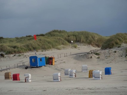 Several beach chairs are standing on the sandy beach in front of a hilly dune landscape and a