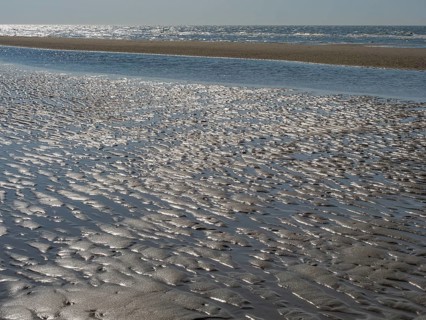 Beach with wavy sand surface and glittering water in front of a wide sea, glittering sea water at