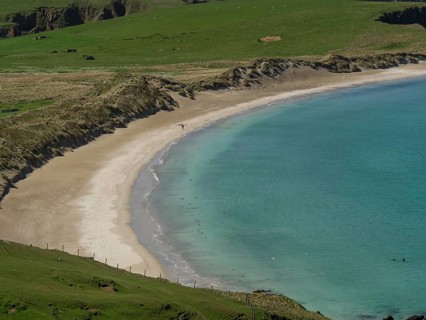 A quiet sandy beach surrounded by rocky cliffs and gentle green slopes, with turquoise clear water