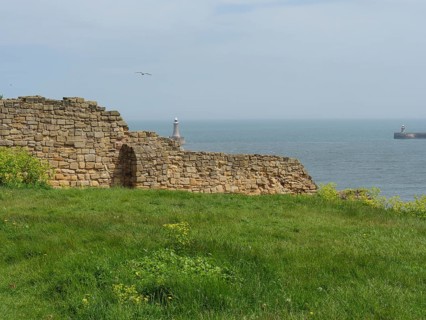 Remains of an old wall in front of a calm sea with a lighthouse in the distance, ruins and old