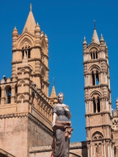 Historic cathedral with detailed towers and a central statue, under a bright blue sky, two red