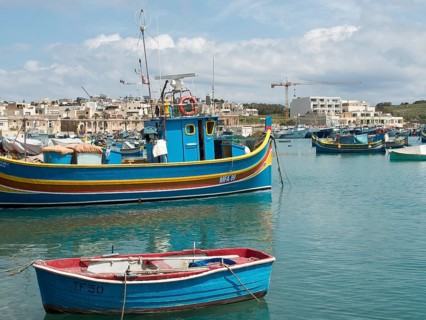 Harbour view with fishing boats and town in the background, a crane is visible, many colourful