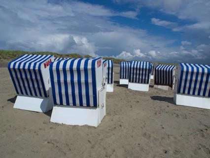 Blue and white beach chairs on the beach in front of dunes and a cloudy sky, blue and white striped