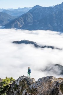 Hiker at Ettaler Manndl, view over mountain landscape and sea of clouds, high fog in the valley,