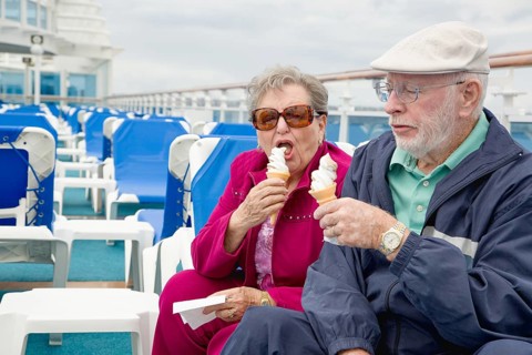 Happy senior adult couple enjoying ice cream on the deck of a luxury passenger cruise ship