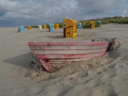 An old boat is buried in the sand, surrounded by colourful beach chairs and cloudy sky, colourful