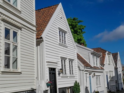 Row of white wooden houses with red tiled roofs under a blue sky, white wooden houses with green