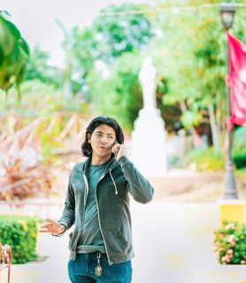 Young man gesturing and talking on the phone in a park. Latin guy talking on cell phone outdoors