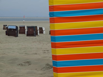 An empty beach with colourful stripes in the foreground and beach chairs in the background, beach