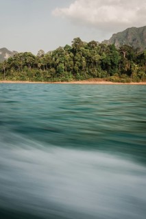 Moving water in front of a picturesque coastline with forest in the background. Khao Sok National