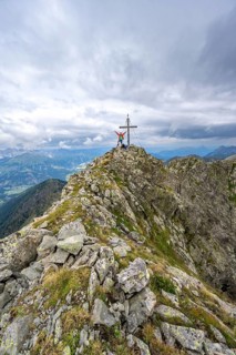Mountaineer stretches his arms in the air, on the rocky pointed summit of the Raudenspitze or Monte