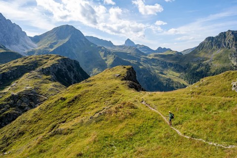 Mountaineer on a hiking trail on a grassy mountain ridge, idyllic mountain landscape with green