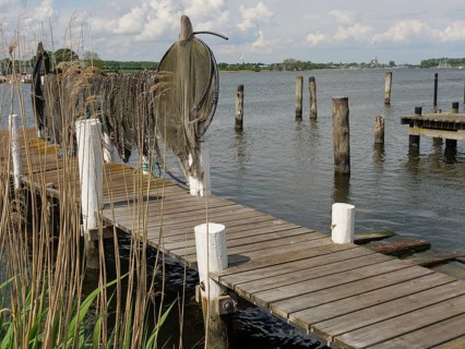 A wooden jetty leads out into the water, lined with fishing nets and surrounded by calm lake shores