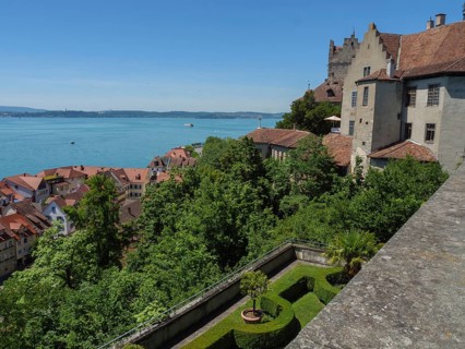 View of a castle with a wide view over roofs and trees to a lake, old buildings with many trees on