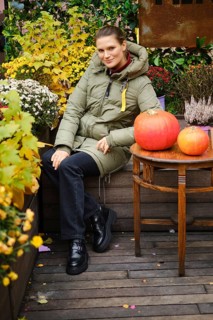 Smiling woman in down jacket sits on bench surrounded with autumn flowers
