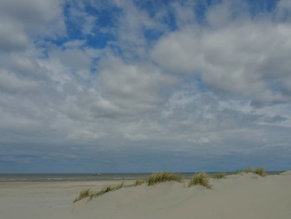 Spacious beach with sand dunes, calm sea and partly cloudy sky, dunes by the sea with clouds in the