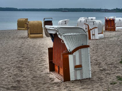 A quiet beach with several beach chairs and a stone quay in the background under a cloudy sky,