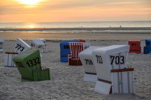 White, red and green beach chairs on a sandy beach at sunset, many colourful beach chairs on a warm