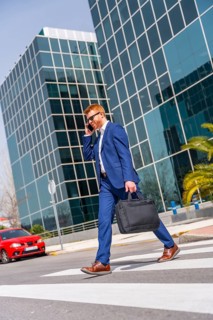 Vertical full length photo of a cool businessman talking to the mobile walking along the city