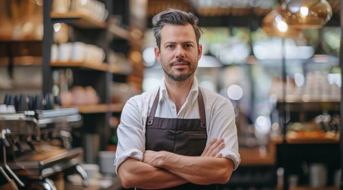 Small business owner stands in front of a counter with apron on and a smile on his face, AI