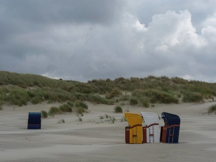 Scattered beach chairs and grey sky over a deserted beach, colourful beach chairs on the beach and