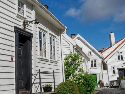 Winding street with white houses, windows, lanterns and a green bush in sunny weather, white wooden
