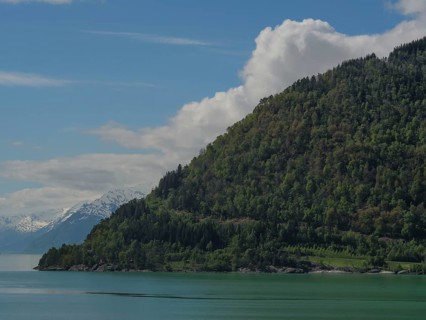 Green mountains at a lake with partly cloudy sky, nature idyll, greenish shimmering water in a