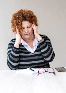 A mid-adult redhead woman with a headache is rubbing her temples. Vertical shot