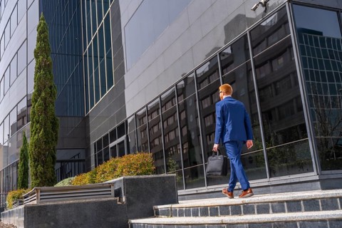 Full length rear view of a businessman with laptop bag and suit walking along a financial district