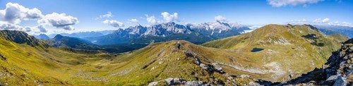Panorama, mountaineer on a hiking trail between green mountain meadows on a mountain ridge,