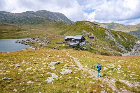 Hiker on hiking trail to Obstanserseehuette, mountain lake Obstansersee between green mountain