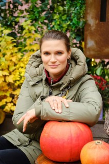 Lovely woman sitting at an autumn fair with her hand on a pumpkin on the table
