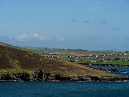 View of a coastal landscape with houses and green hills looking out to sea, green meadows on a deep