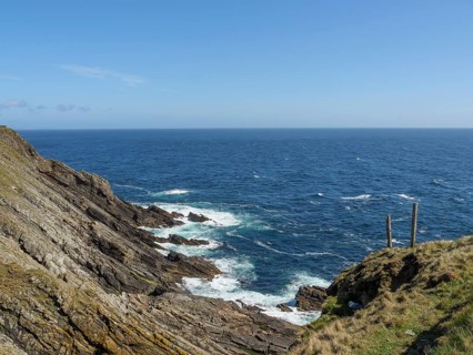 View of a rocky coastline with green grass and blue sea under a clear sky, green meadows on a deep