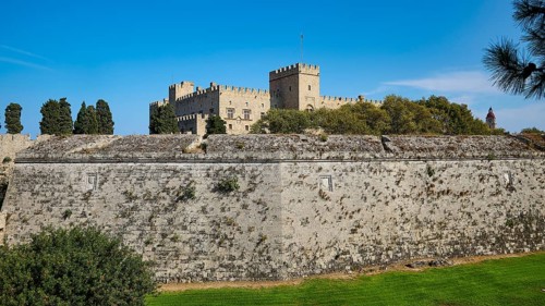 View of a castle across a large stone fortress wall, against a blue sky, Grand Master's Palace,