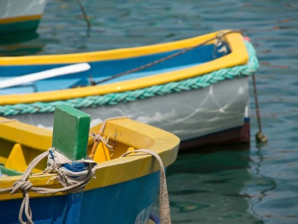 Close-up of a part of a yellow and blue fishing boat in the water, many colourful fishing boats in