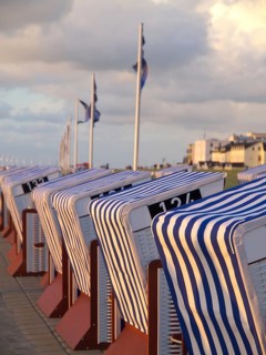 Row of striped beach chairs at sunset by the sea, with buildings and clouds in the background, blue