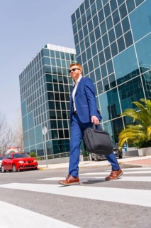 Vertical full length photo with low angle view of an elegant cool businessman crossing the street